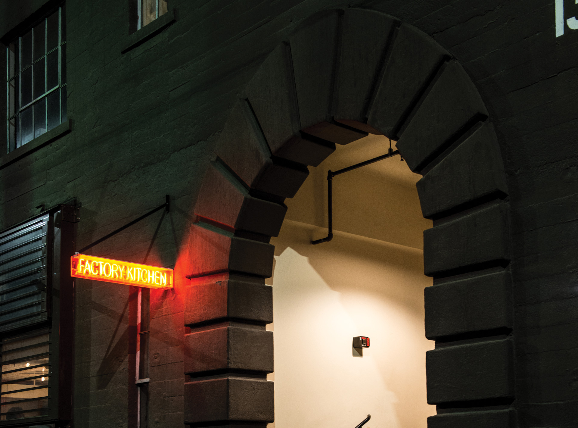 Outdoor night time picture of The Factory Kitchen entrance with Factory Kitchen sign lit up in red
