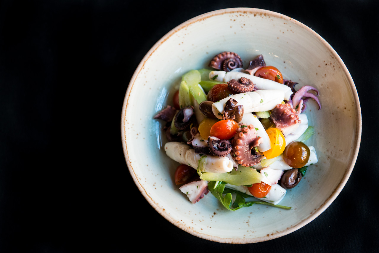Top View of a bowl of our delicious squid salad with cherry tomatoes, celery, Taggia olives, Italian parsley